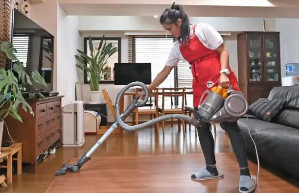 Person vacuuming a living room with a cylinder vacuum cleaner.