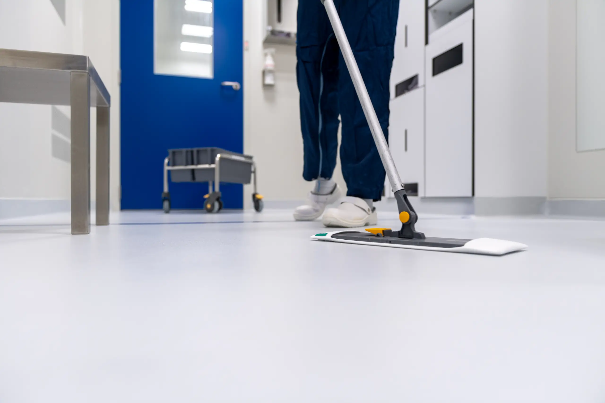 Person mopping a shiny white floor in a clean room with blue doors.