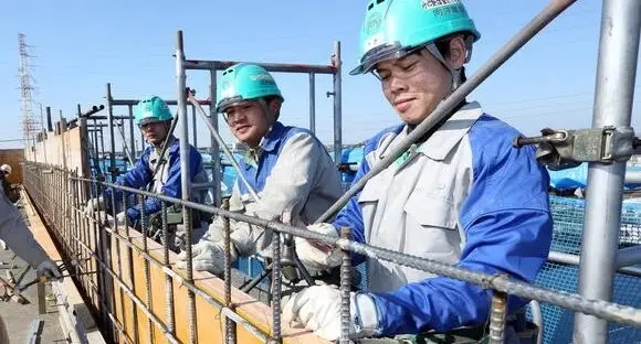 Construction workers in blue uniforms and helmets on a scaffold.
